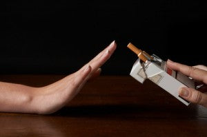 Blog HappeSmoke | Ma cigarette électronique coule! Que faire? Main repoussant un paquet de cigarettes posé sur une table en bois